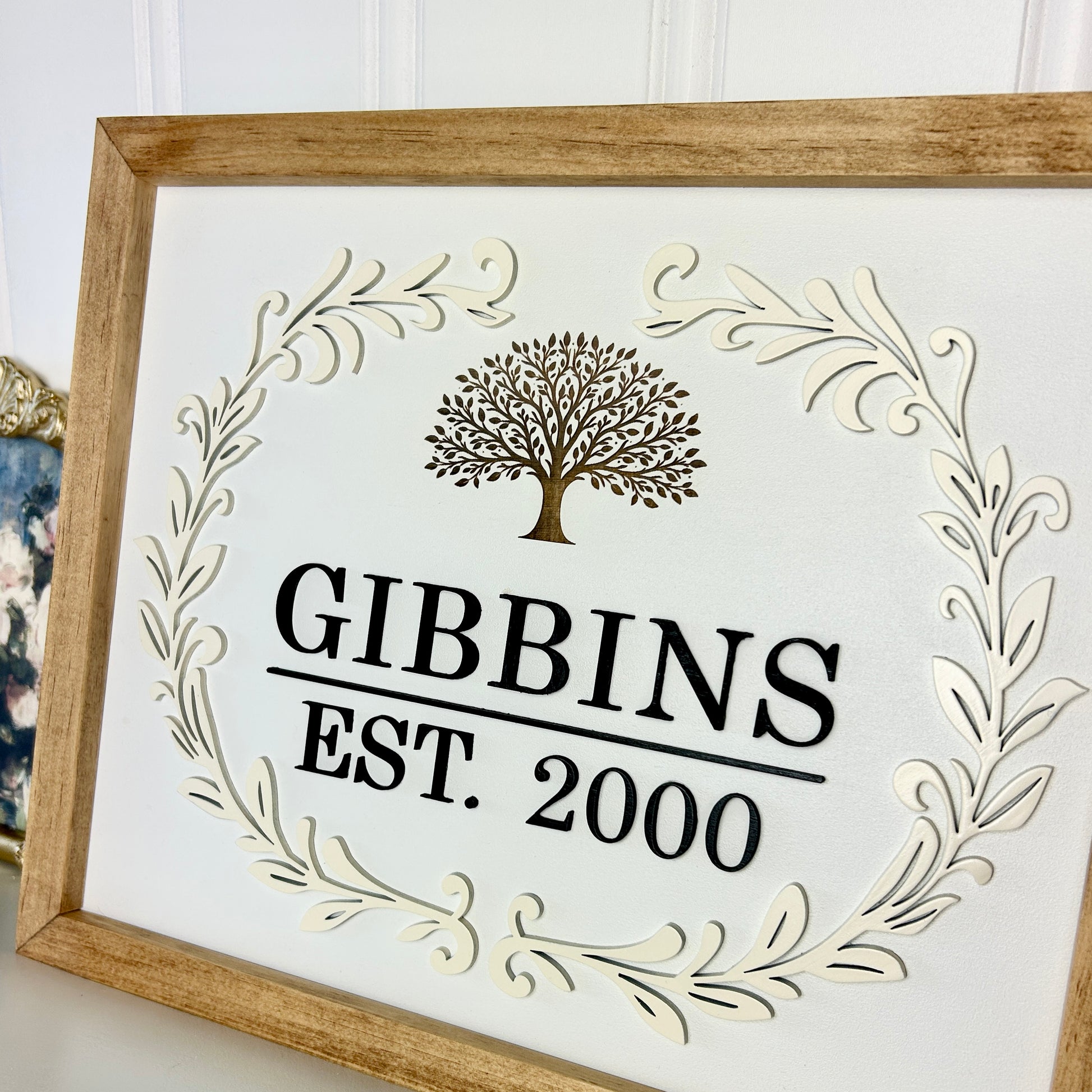 Decorative sign with 'GIBBINS EST. 2000' and tree design in a wooden frame.